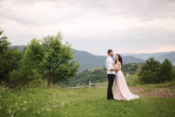 Beautiful young wedding couple standing on the green slope, hill. Groom and bride in Carpathian mountains - Photo, Image