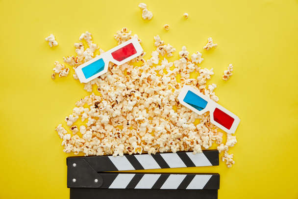 Draufsicht auf köstliches Popcorn, 3D-Gläser und Klappbrett auf gelbem Hintergrund - Foto, Bild