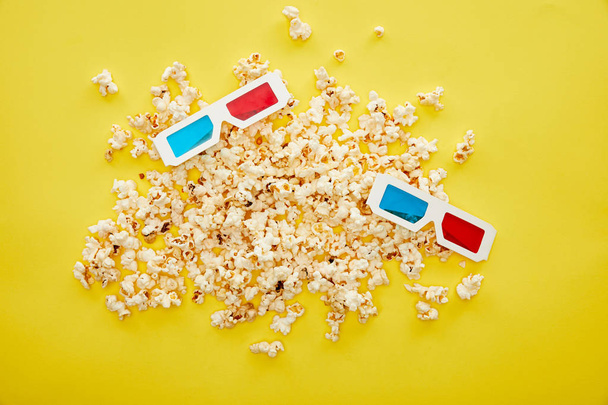 top view of delicious popcorn scattered near 3d glasses on yellow background - Photo, image
