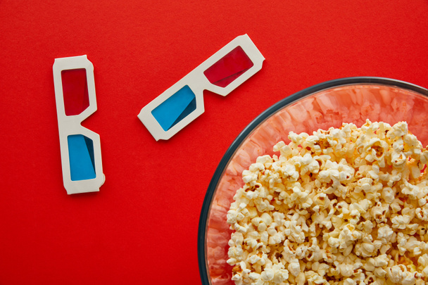 top view of delicious popcorn in bowl near 3d glasses isolated on red - Valokuva, kuva