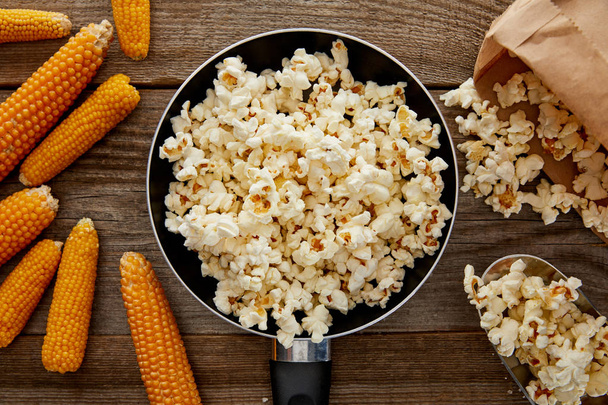 top view of popcorn in frying pan near ripe corn on wooden background - Fotoğraf, Görsel