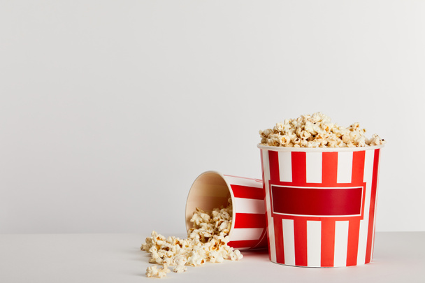 tasty popcorn scattered from red striped paper buckets isolated on grey - Foto, Imagen