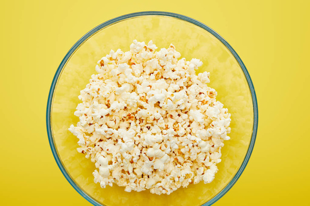 top view of delicious popcorn in glass bowl on yellow background - Fotografie, Obrázek
