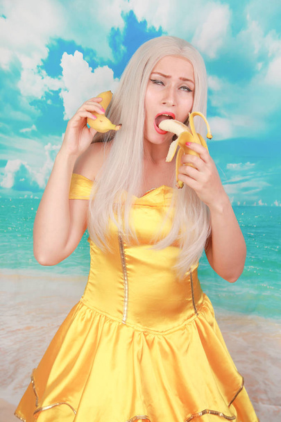 Ładna dziewczyna w Pinup żółta sukienka na niebieskim tle. dieta bananowa. - Zdjęcie, obraz