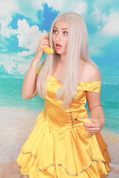 pretty girl in pinup yellow dress on blue background. banana dieting. - Photo, Image