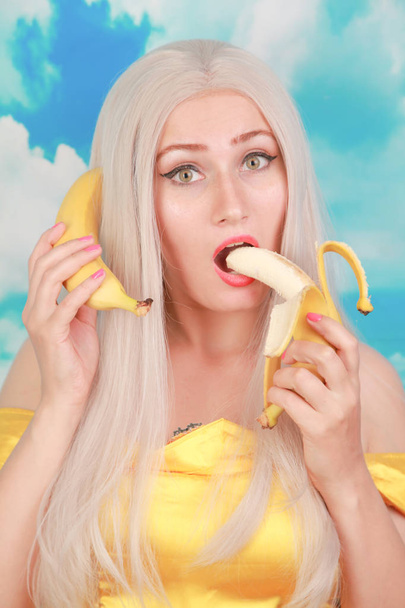 pretty girl in pinup yellow dress on blue background. banana dieting. - Foto, afbeelding