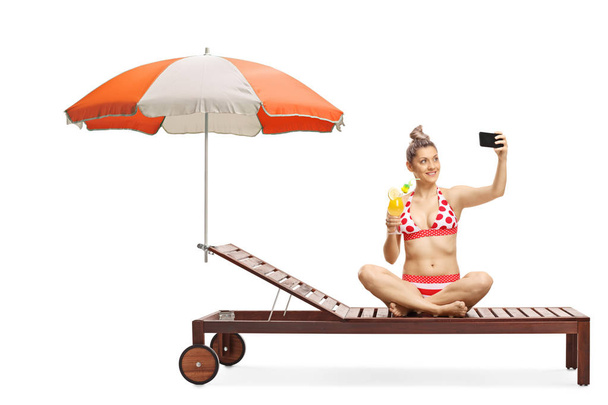 Νέα γυναίκα με μπικίνι κάθεται σε ένα σολάριουμ κάτω από ομπρέλα κρατώντας - Φωτογραφία, εικόνα