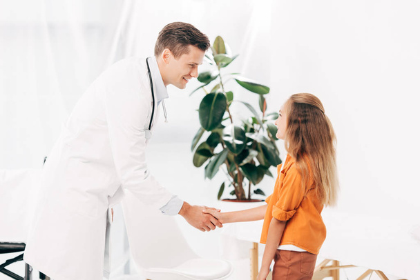 pediatrist in white coat and child shaking hands and looking at each other - Fotoğraf, Görsel