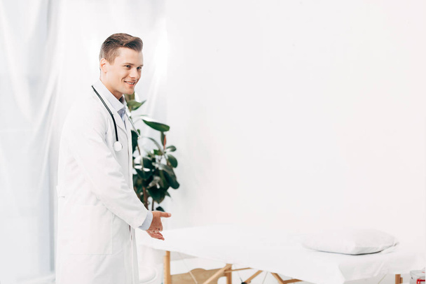 lachende dokter in witte vacht met stethoscoop in kliniek - Foto, afbeelding