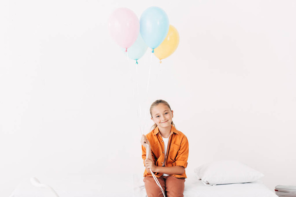 child holding colorful balloons and smiling in hospital - Foto, afbeelding
