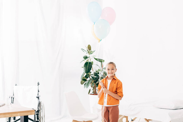 child holding colorful balloons and smiling in hospital - Fotografie, Obrázek