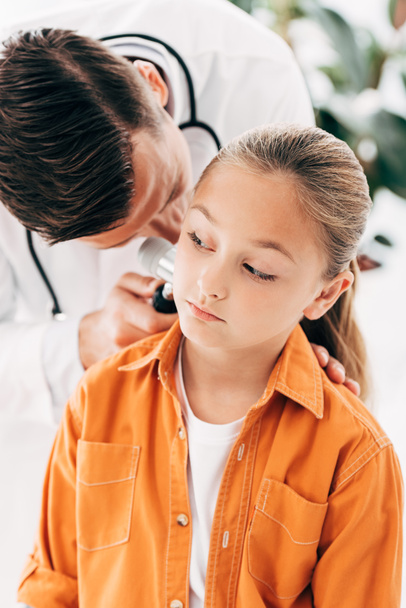 focused pediatrist in white coat examining child with dermascope - Фото, изображение