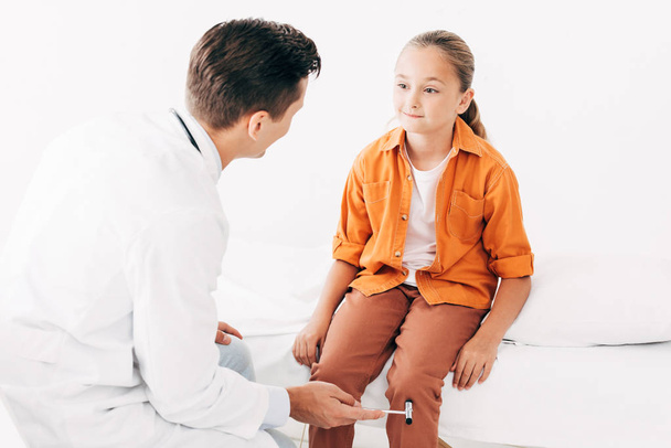 pediatrist σε λευκό παλτό εξέταση παιδί με σφυρί αντανακλαστικό - Φωτογραφία, εικόνα