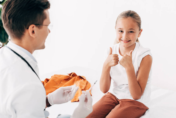 pediatrist strzykawki i uśmiechnięte dziecko pokazuje kciuki w górę - Zdjęcie, obraz