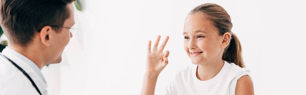 panoramic shot of pediatrist and smiling child showing okay sign - Фото, изображение