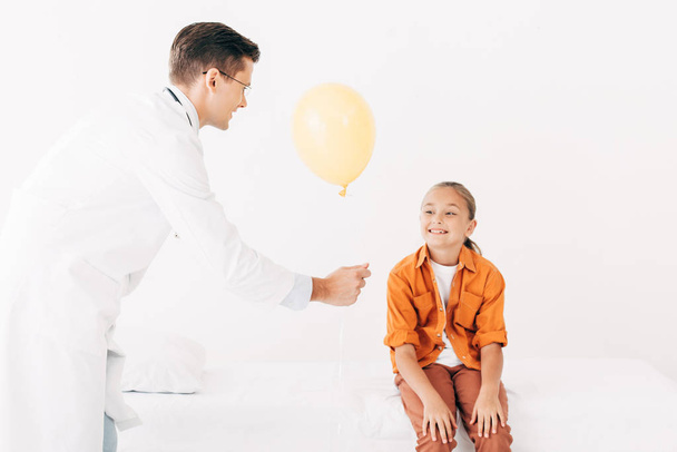 Kinderarzt im weißen Kittel gibt Kind in Klinik gelben Luftballon - Foto, Bild