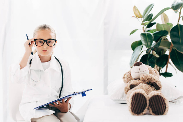 front view of child in doctor costume holding clipboard and pen in clinic - 写真・画像
