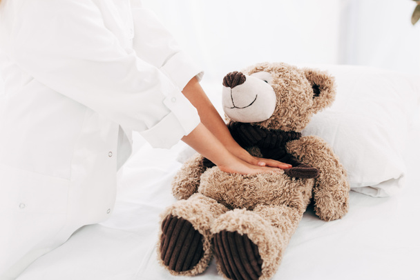 partial view of kid in doctor costume doing heart massage to teddy bear - Photo, image