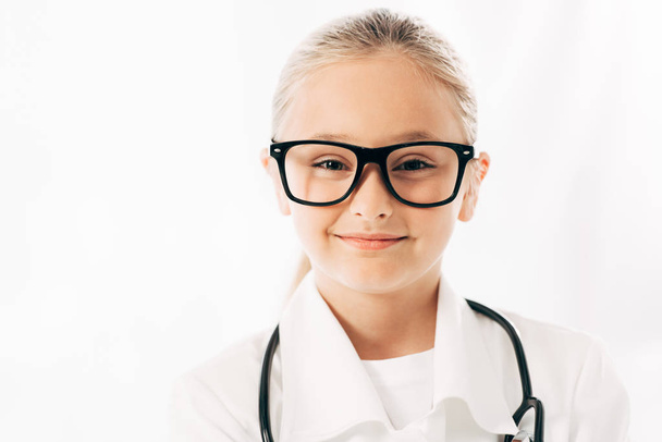 Frontansicht eines lächelnden Kindes in Arztkostüm und Brille, das isoliert auf weiß in die Kamera blickt - Foto, Bild