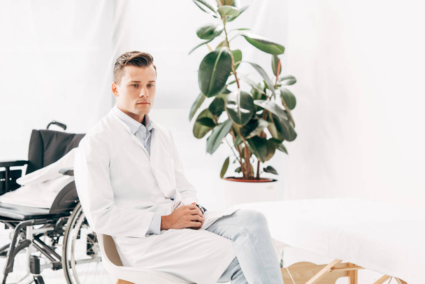 pensive doctor in white coat sitting with clenched hands - Foto, afbeelding
