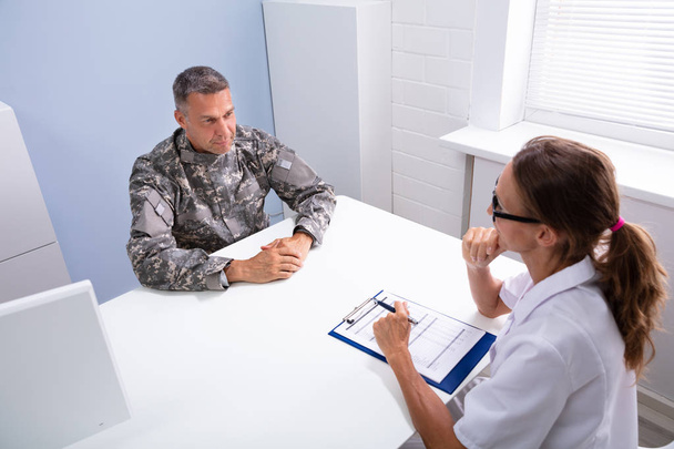 Female Doctor And Worried Military Officer Discussing About Problems He Has During Psychotherapy Treatment - Foto, Imagem