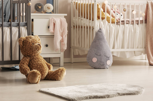 Close-up of a cute teddy bear and a gray raindrop pillow on the floor of a scandi bedroom interior for twins. Real photo - Foto, imagen