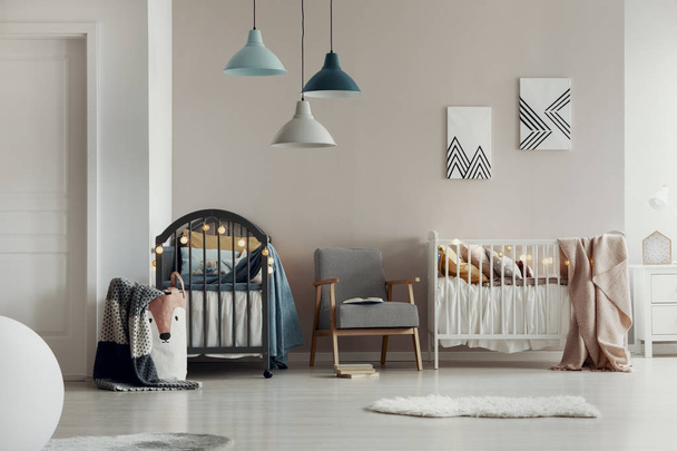Real photo of a spacious, white and beige bedroom interior for twins with two wooden cribs and an armchair - Valokuva, kuva