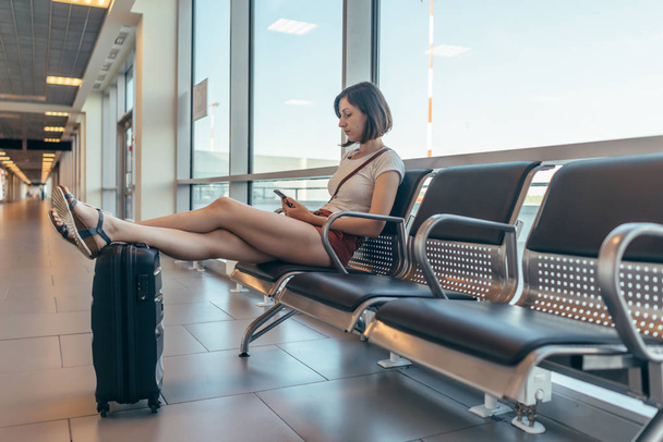 Turista sentada en el banco con equipaje en la sala de espera en el aeropuerto
. - Foto, imagen