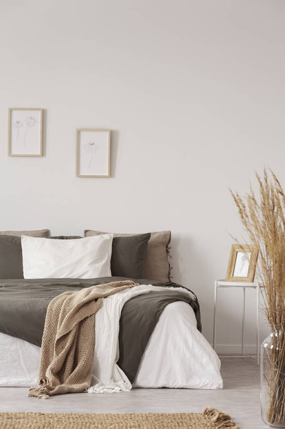 Graphics in wooden frames on white empty copy space wall in bedroom with comfortable bed with black and grey pillows and duvet - Φωτογραφία, εικόνα