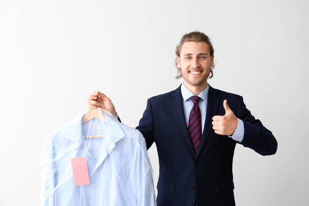 Businessman with clothes after dry-cleaning showing thumb-up on white background - Φωτογραφία, εικόνα