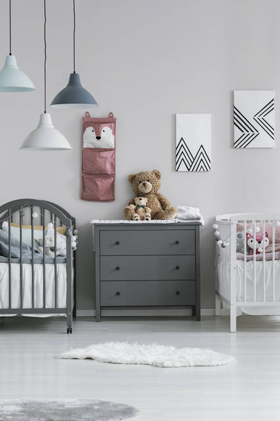 Simple, gray and white room interior for two little children with a chest of drawers between two wooden beds. Real photo - Foto, Imagem