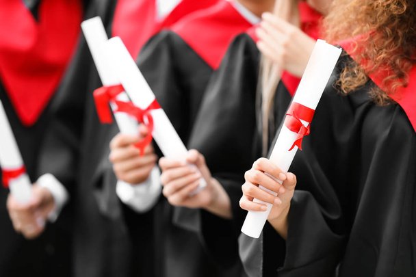 Молодые студенты в холостяцких одеждах и с дипломами на открытом воздухе
 - Фото, изображение