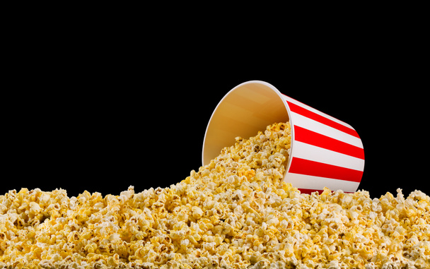 Scattered popcorn from paper striped bucket isolated on black background - Foto, immagini