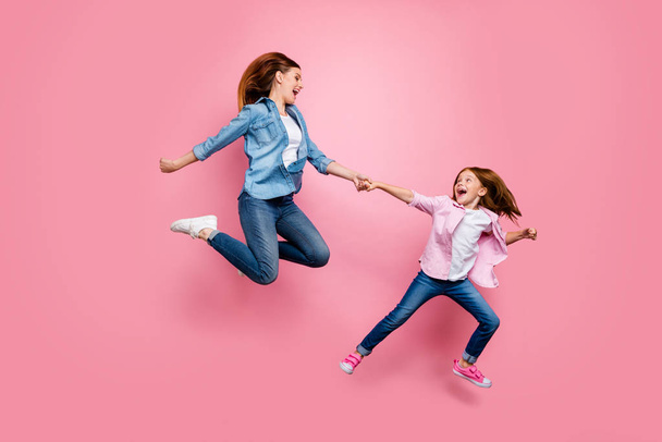 Photo of foxy little lady and her excited mom jumping high walking toy shop wear casual jeans outfit isolated pink background - Fotografie, Obrázek