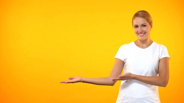 Young smiling woman presenting template on orange background, announcement - Fotografie, Obrázek