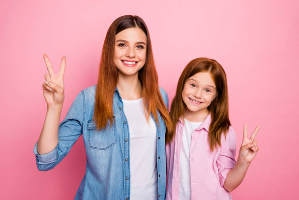 Portrait of cheerful girls with long hair making v-signs wearing denim jeans shirts isolated over pink background - Fotografie, Obrázek