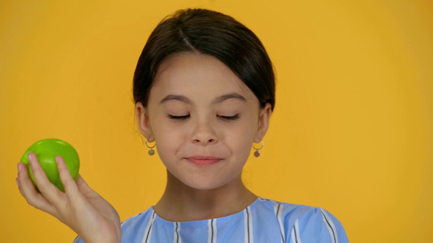 doordachte kind bijten groene appel en glimlachend geïsoleerd op geel - Video