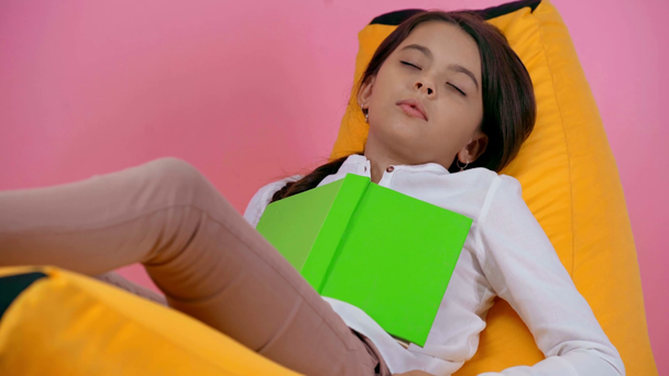 child sleeping with book on bean bag chair isolated on pink - Filmati, video