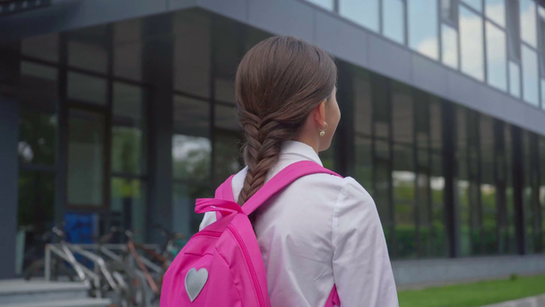 Achteraanzicht van schoolmeisje met rugzak wandelen op schoolplein - Video