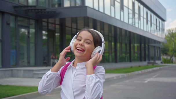 Gelukkig schoolmeisje luisteren muziek in koptelefoon op schoolplein - Video