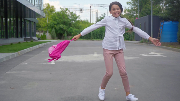 щаслива збуджена школярка кружляє з рюкзаком на шкільному подвір'ї
 - Кадри, відео