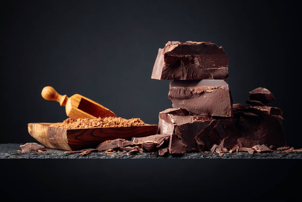 Zwarte chocolade en houten schaaltje met cacaopoeder op een donkere rug - Foto, afbeelding