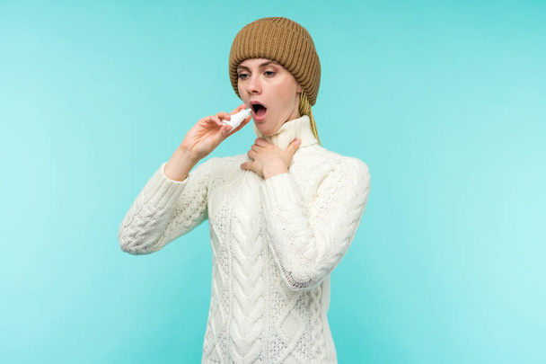 Chory młoda kobieta w szalik i kapelusz używać aerozol do nosa na białym tle - Zdjęcie, obraz