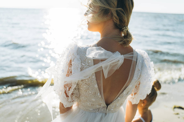 back view of stylish bride standing on the beach at the sunset  - Foto, imagen