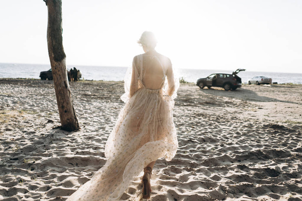 back view of young woman in long dress walking on the beach, full length shot - Foto, imagen