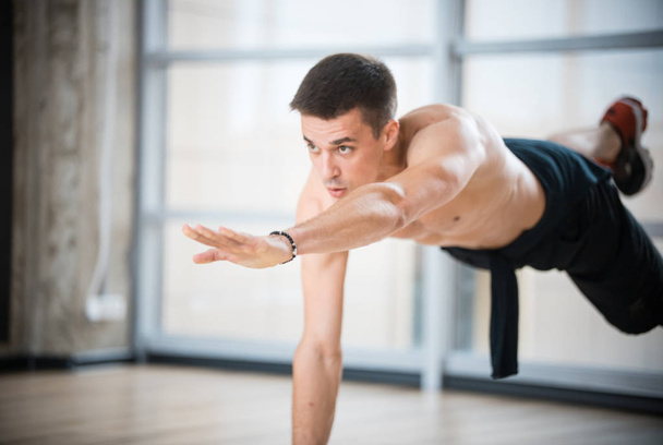ein athletischer Mann mit nacktem Oberkörper beim Training im Studio - einerseits stehend - Foto, Bild