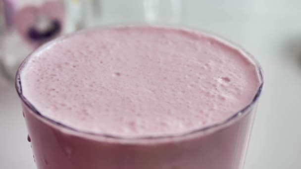 Pink milkshake in a transparent glass in which bubbles burst, close-up, natural light - Metraje, vídeo