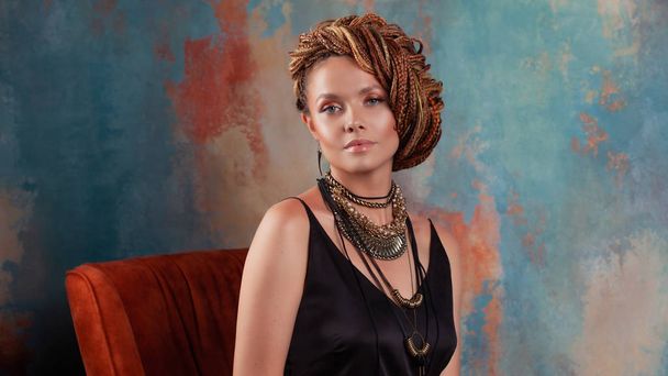Southern flavor. Stylish beautiful young woman with afro braids tucked into high hair, sitting in chair in warm colors. - Foto, afbeelding
