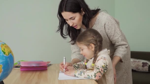Mother helps her little daughter to make homework at home. Young woman shows a girl how to write correctly in exercise book. The mother spend her leisure time helping her first-grade daughter to study. Prores codec. - Footage, Video