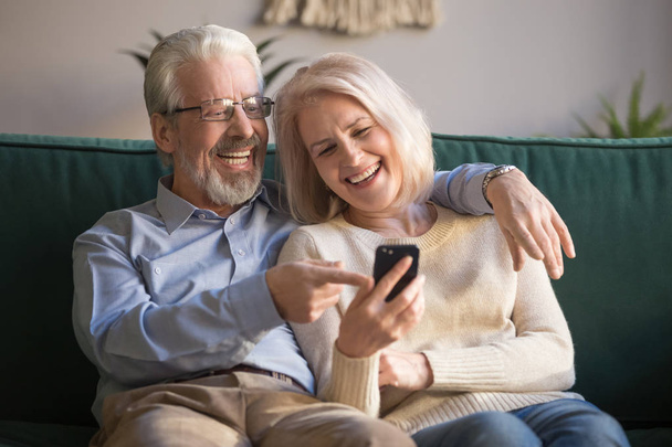 Feliz pareja de edad sosteniendo teléfono inteligente mirando la pantalla del teléfono móvil riendo
 - Foto, Imagen
